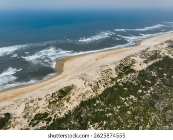 Luchtfoto van een schoon zandstrand met witte duinen en weelderige vegetatie aan de blauwe oceaan.