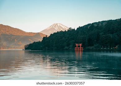 Pemandangan indah Gunung Fuji di sebalik hutan rimbun dan pintu gerbang torii merah ikonik di Tasik Ashi di Hakone, Jepun semasa matahari terbit. Teks jepun pada pintu gerbang torii diterjemahkan kepada "Kuil Kuzuryu".