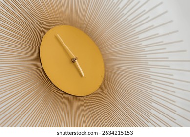 Une horloge murale moderne avec un cadran circulaire doré, des aiguilles minimalistes et des tiges métalliques rayonnantes, montée sur un fond blanc uni.