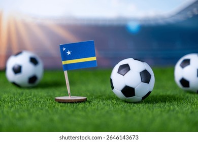 サッカーボールが置かれた緑の人工芝の上に置かれたキュラソー島のミニチュア国旗のクローズアップ。これは、代表チームが世界的なスポーツイベントに参加することを示している。