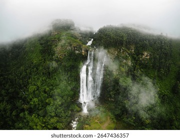 Slikovita fotografija dronom snimljena na slapu Lovers Leap, skrivenom prirodnom dragulju u Nuwara Eliyi na Šri Lanki, koji se spušta kroz maglovitu gorsku džunglu. Savršeno za eko-putovanja i promocije s temom prirode.