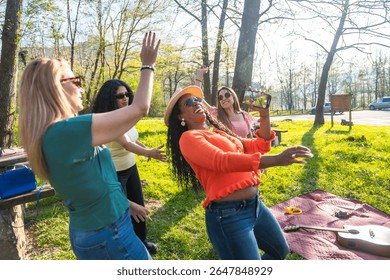 Vier Frauen unterschiedlicher Herkunft tanzen und haben Spaß in einem Park, eine von ihnen filmt mit ihrem Handy.