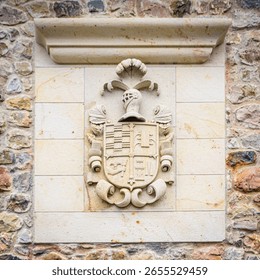 Um brasão de família ornamentado está esculpido em uma placa de pedra clara encostada na parede rústica de uma aldeia no Vale do Cabuerniga, na Cantábria.
