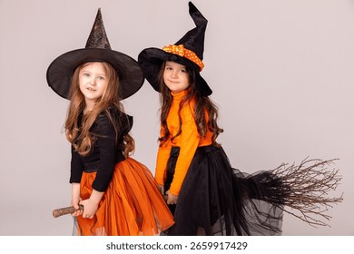 Dwie małe dziewczynki w strojach czarownic bawią się w Halloween i latają na miotle na białym tle z miejscem na tekst. Dzieciaki chodzą po cukierki. Koncepcja imprezy halloweenowej.