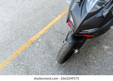 Vooraanzicht van een matzwarte en rode sportmotorfiets geparkeerd op straat met een grijze muur als achtergrond, perfect voor stedelijke autoconcepten