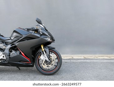 Vooraanzicht van een matzwarte en rode sportmotorfiets geparkeerd op straat met een grijze muur als achtergrond, perfect voor stedelijke autoconcepten