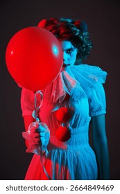 Concept vechi de circ. Portretul unei clovne într-un costum alb de circ, care stă pe un fundal întunecat și sumbru și își ascunde fața în spatele unui balon roșu. Halloween înfricoșător.
