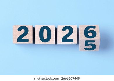 Bonne année 2026. Cube en bois passant de 2025 à 2026 sur fond bleu. Concept de fond pour le Nouvel An 2026. Affaires, résolutions, objectifs, inspiration, réussite, idées.