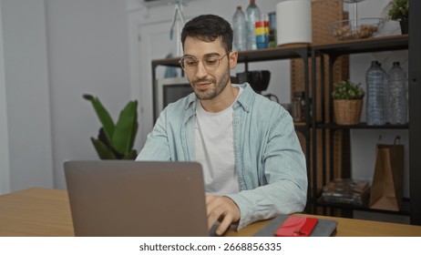 Jovem hispânico trabalhando em um laptop em um escritório moderno com prateleiras, plantas e artigos de papelaria, criando uma atmosfera de trabalho aconchegante e profissional.