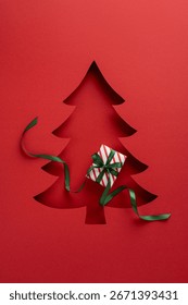 Carte de vœux verticale rouge artistique représentant un sapin de Noël découpé et une boîte cadeau rayée. Sa composition élégante évoque l'esprit festif et la joie des fêtes.