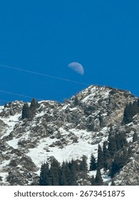 Zasnežen gorski vrh pod jasnim modrim nebom, nad katerim žari polmesec, čez prizor pa potekajo daljnovodi.