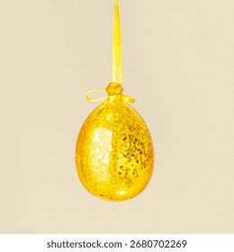 Decoración navideña: bola dorada brillante con cinta amarilla sobre fondo beige, tendencia minimalista de Año Nuevo. Adorno navideño amarillo de temporada, vista lateral, como elegante tarjeta navideña monocromática, con espacio de copia.