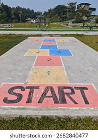 Juego de rayuela colorido pintado sobre hormigón en un patio de juegos al aire libre, con números y un gran cartel de INICIO, que simboliza la infancia, el juego y la recreación.