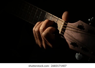 Gros plan cinématographique sur la main d'un musicien pinçant un accord sur une guitare acoustique sous un éclairage tamisé et dramatique, créant une ambiance émotionnelle