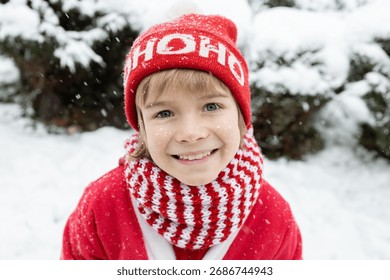 Ritratto di un grazioso bambino in un costume rosso da Babbo Natale in un inverno innevato all'aperto. Aiutante di Babbo Natale. Felice Anno Nuovo e Buon Natale. Vacanze invernali, infanzia felice.
