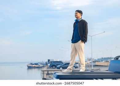 Ein asiatischer Mann, der auf einer Autoreise unterwegs ist und Musik hört, genießt die schöne Landschaft, das ruhige Meer, den blauen Himmel und das ruhige Meer während eines Sommerabenteuers in Thailand, während er auf der Ladefläche eines Pick-ups sitzt.