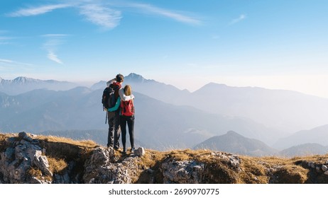 Una coppia è in piedi su una cima rocciosa e ammira la vista mozzafiato sulle montagne mentre il sole inizia a sorgere.