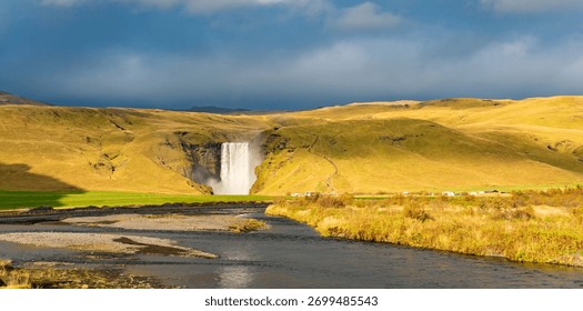 Vodopad Skogafoss na Islandu se spušta niz strmu liticu, stvarajući snažnu maglu koja formira živopisnu dugu. Okolni bujni zeleni krajolik naglašava njegovu veličanstvenu ljepotu.