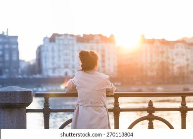 Una mujer joven está mirando la puesta de sol sobre un río en la ciudad de Praga con los edificios antiguos al fondo. Muelle suave retroiluminado. Imagen en tonos de color.