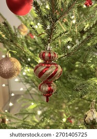 Ornament de Crăciun auriu și roșu atârnat pe un brad decorat cu lumini calde și strălucitoare. Atmosferă de sărbătoare confortabilă, plină de spiritul magiei Crăciunului și Anului Nou.