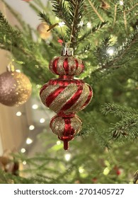 Ornament de Crăciun auriu și roșu atârnat pe un brad decorat cu lumini calde și strălucitoare. Atmosferă de sărbătoare confortabilă, plină de spiritul magiei Crăciunului și Anului Nou.