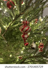 Ornament de Crăciun auriu și roșu atârnat pe un brad decorat cu lumini calde și strălucitoare. Atmosferă de sărbătoare confortabilă, plină de spiritul magiei Crăciunului și Anului Nou.