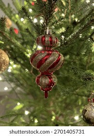 Ornament de Crăciun auriu și roșu atârnat pe un brad decorat cu lumini calde și strălucitoare. Atmosferă de sărbătoare confortabilă, plină de spiritul magiei Crăciunului și Anului Nou.