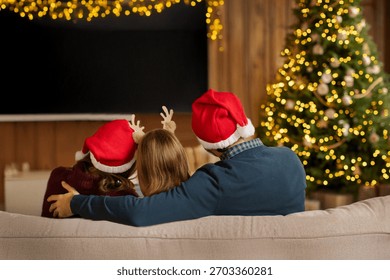Familie în pălării de Moș Crăciun vizionând un film pe ecranul de proiecție de pe peretele camerei decorate pentru Crăciun, vedere din spate. Concept de echipament TV acasă