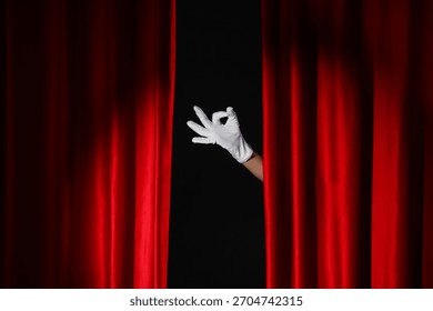 Female hand in glove showing OK behind red curtains on black background