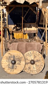 Banca ao ar livre em uma feira medieval exibindo ferramentas tradicionais de marcenaria e dois grandes escudos de madeira com entalhes históricos. Conceito de artesanato, história e mercado de rua.