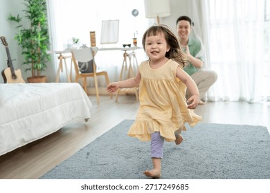 Une petite fille joyeuse joue et court avec son père aimant dans la maison. Adorable bébé, elle s'amuse et prend plaisir à jouer avec son père, un homme mûr et attentionné, dans le salon confortable de leur maison.