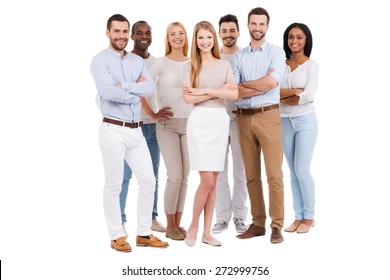 Stolz ein Team zu sein. Volle Länge der multiethnischen Gruppe von Leuten in der intelligenten Freizeitkleidung, die Kamera betrachtet und lächelt, während sie gegen weißen Hintergrund steht