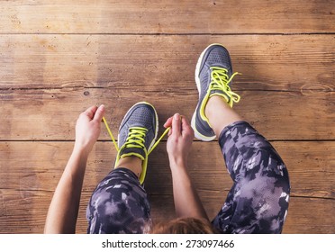 Unrecognizable young runner tying her shoelaces. Studio shot on wooden floor background.