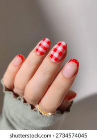 Playful red and pink picnic-style nail art. Features a mix of red gingham checkered patterns, french tips with white polka dots, and classic red accents on rounded nails.