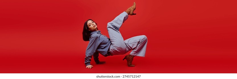 A young beautiful woman showcases her fashion sense with an artistic pose on a bold red background.