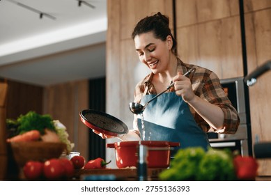 A joyful woman enjoying her time cooking in a modern kitchen. Surrounded by fresh vegetables, she uses a red pot and ladle to prepare a meal, exemplifying the art of home cooking and culinary creativity.