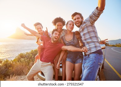 Gruppe von Freunden, die bei Sonnenuntergang mit dem Auto auf der Küstenstraße stehen
