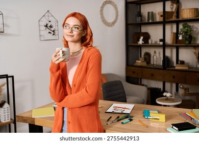 Young woman with red hair savors a warm drink in her stylish cozy home, surrounded by art supplies.