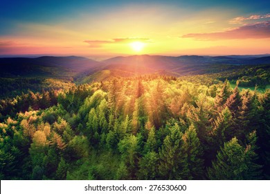 Vogelperspektive eines malerischen Sonnenuntergangs über den Waldhügeln, mit getönten dramatischen Farben