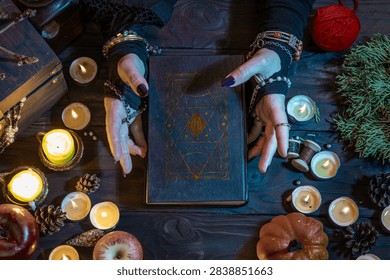 Les mains d'une sorcière, manipulant un grimoire de sorcier, jettent un sort parmi les bougies et les citrouilles la nuit d'Halloween.