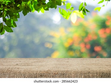 Naturhintergrund und Tischholz für Produktanzeigeschablone, leerer Holztisch und Sacktischdecke über unscharfem grünem Baum im Park, Garten im Freien mit Bokeh-hellem Hintergrund