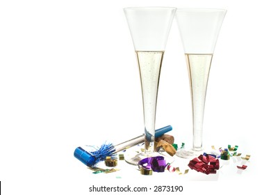 Rayakan Tahun Baru dengan bersulang sampanye! Dua seruling sampanye dengan confetti dan pembuat kebisingan di tanah putih dengan beberapa refleksi.