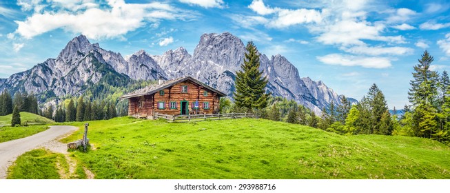 Panoramic view of scenic mountain landscape in the Alps with traditional old mountain chalet and fresh green meadows in springtime