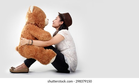 Süßes asiatisches Mädchen, das einander zu einer Teddybärpuppe auf ihrem Schoß schaut, über weißem Hintergrund für Kopierraum