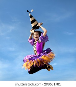 Cute Emotional Little Girl in a Costume of Witch Jumping at the Blue Sky.