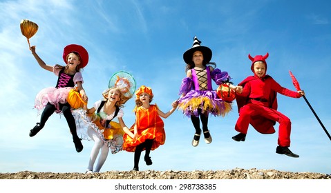 Five Happy Children Running Together to Trick or Treat in the Halloween Costumes of Witches and Devil at the Blue Sky.
