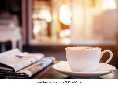 Cup of cappuccino with newspaper on the table, coffee shop background, warm tone