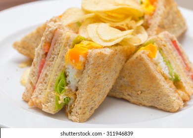 Sekelompok sandwich klub dengan telur goreng, ham, dan mentega keju di atas roti putih.