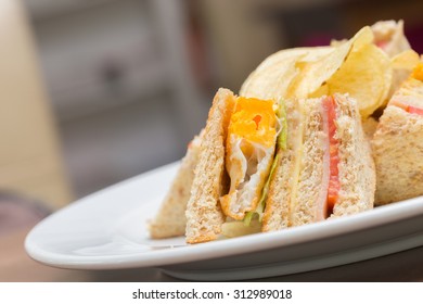 Sekelompok sandwich klub dengan telur goreng, ham, dan mentega keju di atas roti putih.