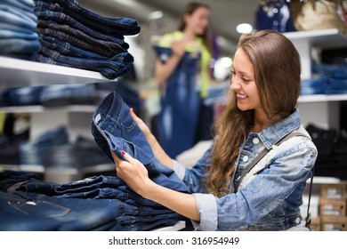 Alegre sonriente joven de pelo largo eligiendo nuevos jeans en la tienda